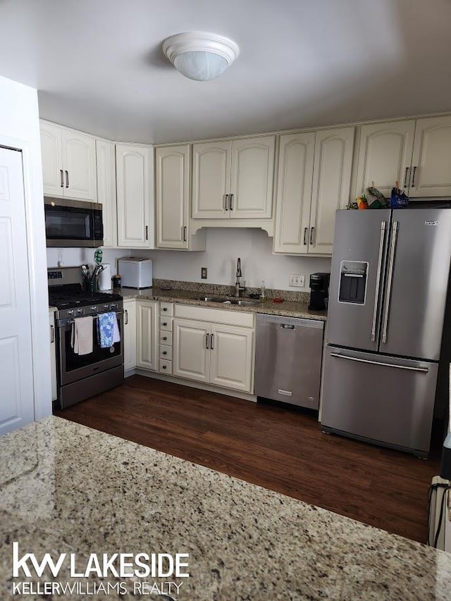 kitchen featuring a sink, light stone countertops, appliances with stainless steel finishes, and dark wood-style floors