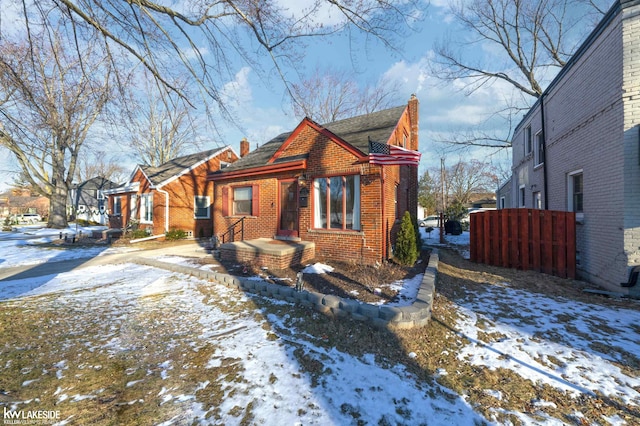 view of front of home with brick siding, a chimney, and fence