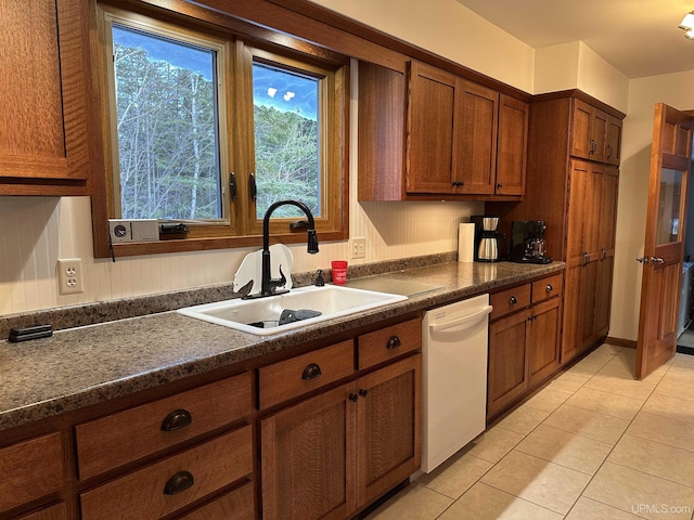 kitchen featuring dark countertops, brown cabinets, white dishwasher, light tile patterned flooring, and a sink