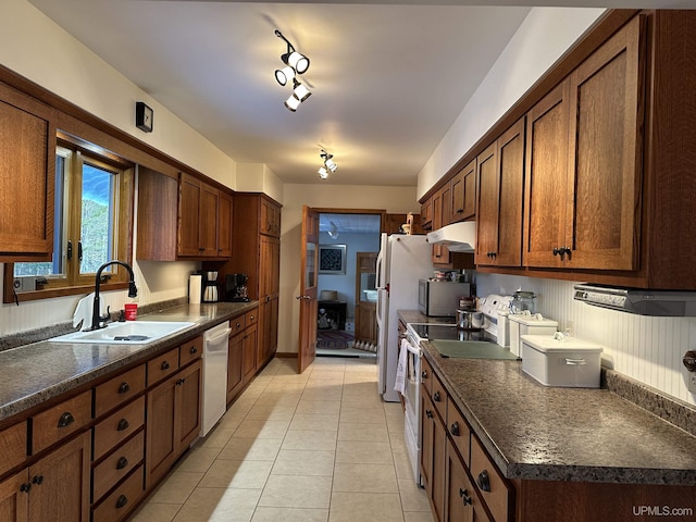 kitchen with a sink, under cabinet range hood, dark countertops, white appliances, and light tile patterned floors