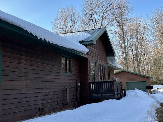 view of snowy exterior featuring an outdoor structure, a detached garage, and metal roof