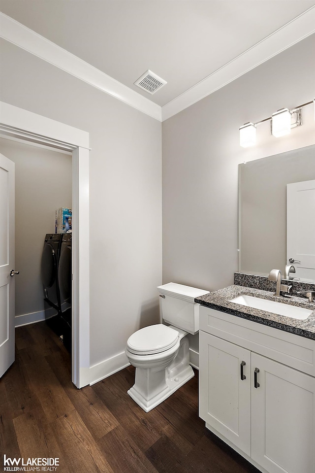 half bathroom with visible vents, independent washer and dryer, wood finished floors, and ornamental molding