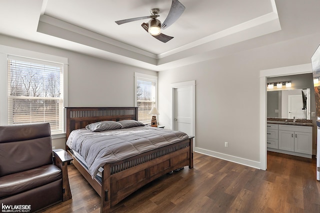 bedroom with ensuite bathroom, a sink, a tray ceiling, dark wood finished floors, and baseboards