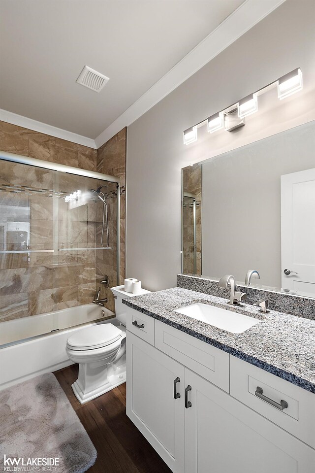 bathroom with vanity, wood finished floors, visible vents, enclosed tub / shower combo, and toilet