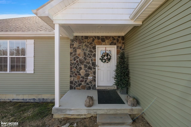 entrance to property featuring stone siding and roof with shingles