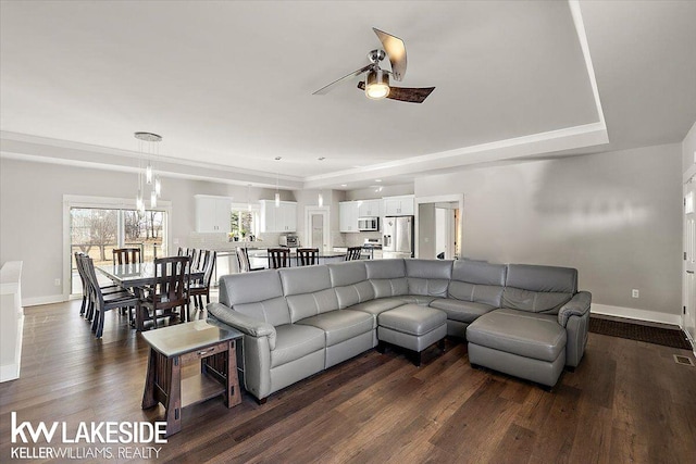 living area featuring dark wood finished floors, visible vents, baseboards, and a ceiling fan