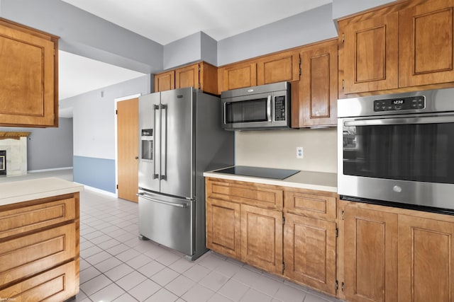 kitchen with stainless steel appliances, light tile patterned flooring, brown cabinetry, and light countertops