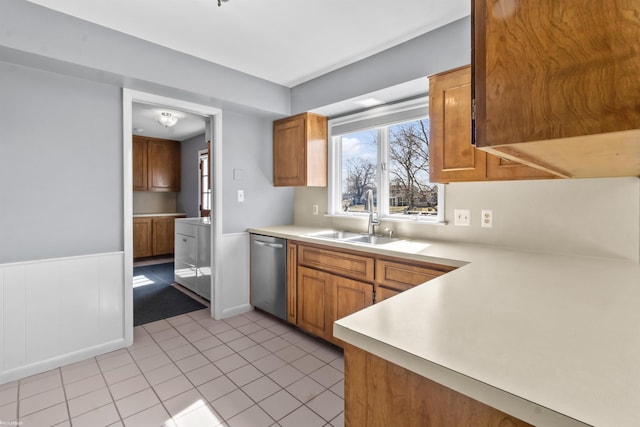 kitchen with a sink, dishwasher, brown cabinetry, and light countertops