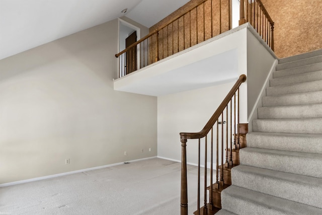 stairway featuring a high ceiling, baseboards, and carpet floors