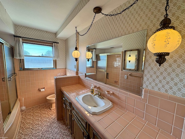 full bathroom featuring toilet, tile walls, vanity, and wallpapered walls