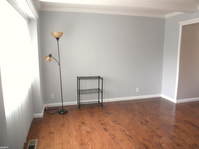 empty room featuring baseboards, wood finished floors, visible vents, and ornamental molding