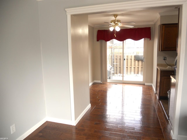 unfurnished dining area featuring crown molding, dark wood-style floors, baseboards, and ceiling fan