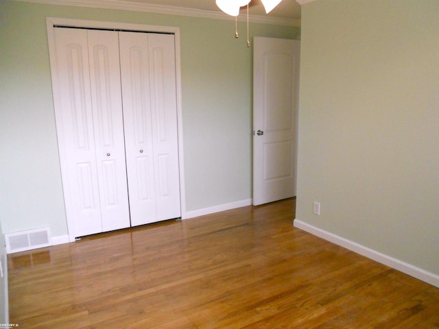 unfurnished bedroom featuring visible vents, a closet, wood finished floors, and crown molding