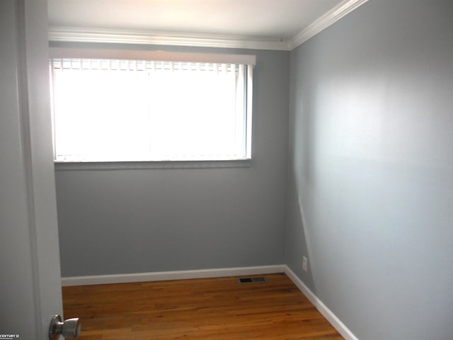 empty room with visible vents, crown molding, wood finished floors, and baseboards