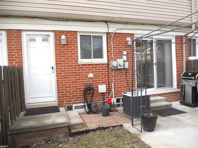 doorway to property with brick siding, cooling unit, and fence