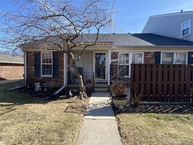 view of front facade with brick siding, a shingled roof, a front lawn, and fence