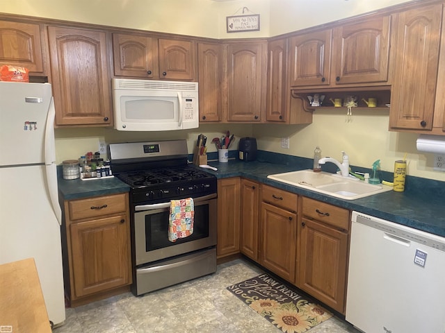 kitchen with a sink, white appliances, dark countertops, and brown cabinets