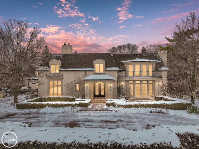 french country inspired facade featuring stucco siding, a balcony, french doors, and a chimney