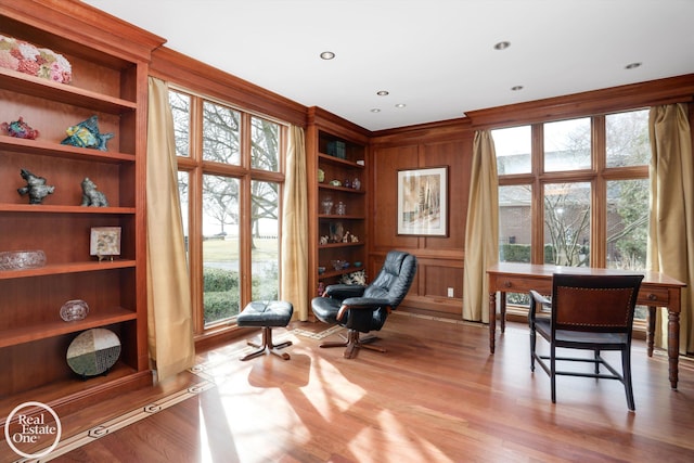 sitting room featuring wooden walls, built in features, wood finished floors, and ornamental molding