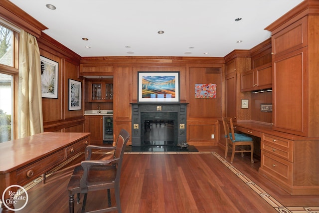 office area featuring wooden walls, beverage cooler, a premium fireplace, built in desk, and wood finished floors