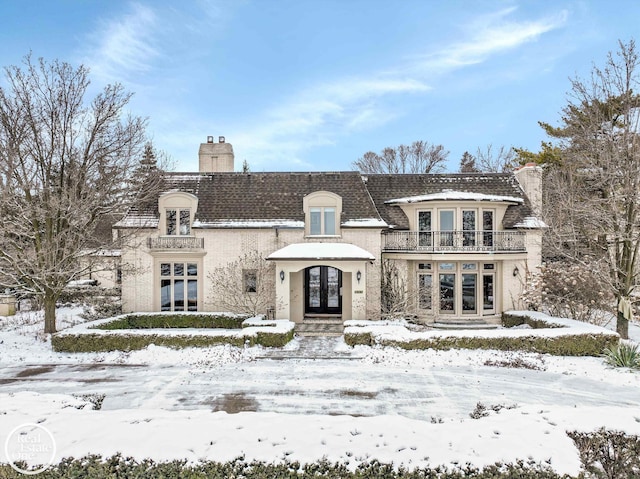 french provincial home with french doors, a balcony, and a chimney