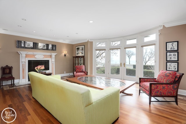 living area with a high end fireplace, wood finished floors, baseboards, and ornamental molding