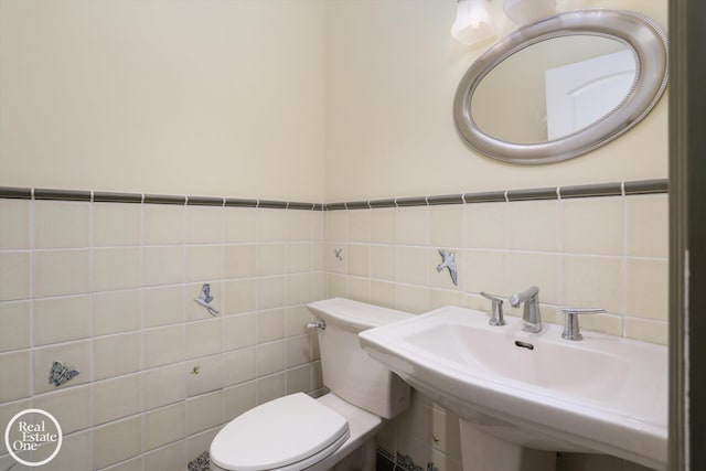 half bathroom with a sink, toilet, tile walls, and wainscoting