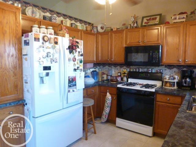 kitchen with dark countertops, white refrigerator with ice dispenser, range with gas cooktop, and black microwave