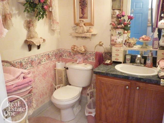 bathroom with tile patterned flooring, wallpapered walls, toilet, and vanity