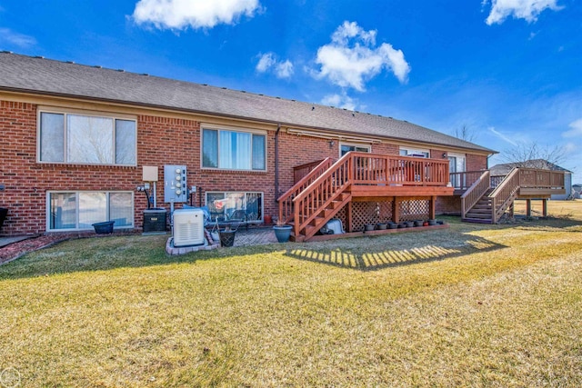 rear view of property featuring a deck, a yard, roof with shingles, brick siding, and stairs