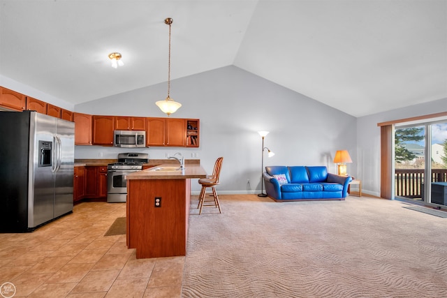 kitchen featuring brown cabinetry, a sink, stainless steel appliances, decorative light fixtures, and open floor plan