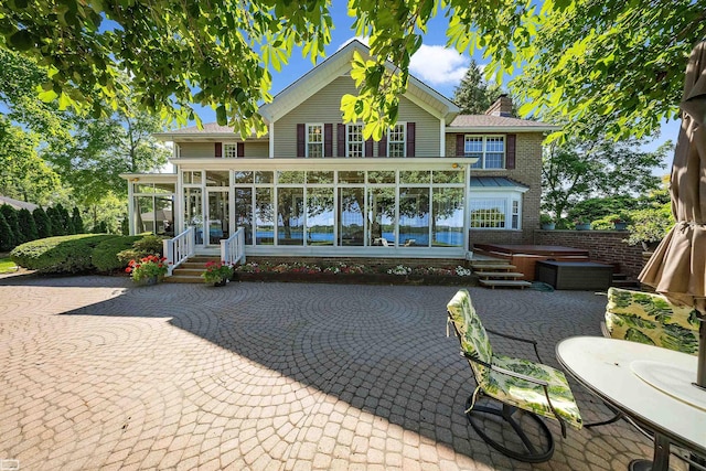 back of property with a patio, brick siding, a sunroom, and a chimney