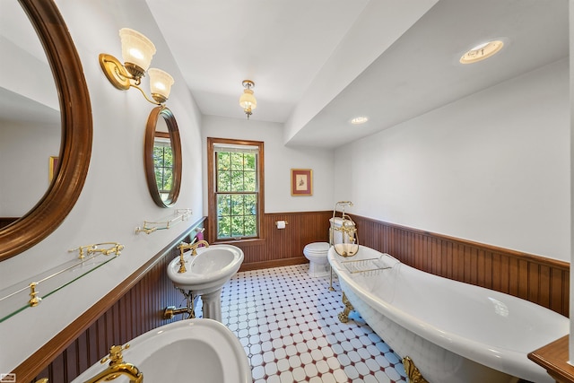 full bathroom with a wainscoted wall, a sink, a freestanding bath, wood walls, and toilet