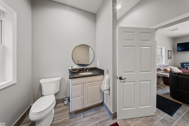 bathroom with toilet, connected bathroom, vanity, baseboards, and wood tiled floor