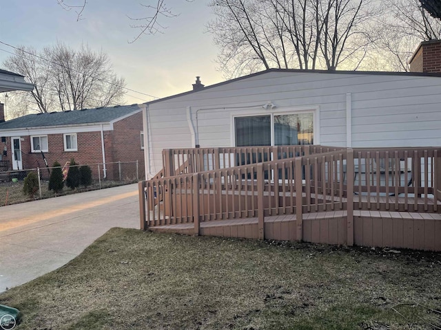 back of property at dusk featuring brick siding, a chimney, and a wooden deck