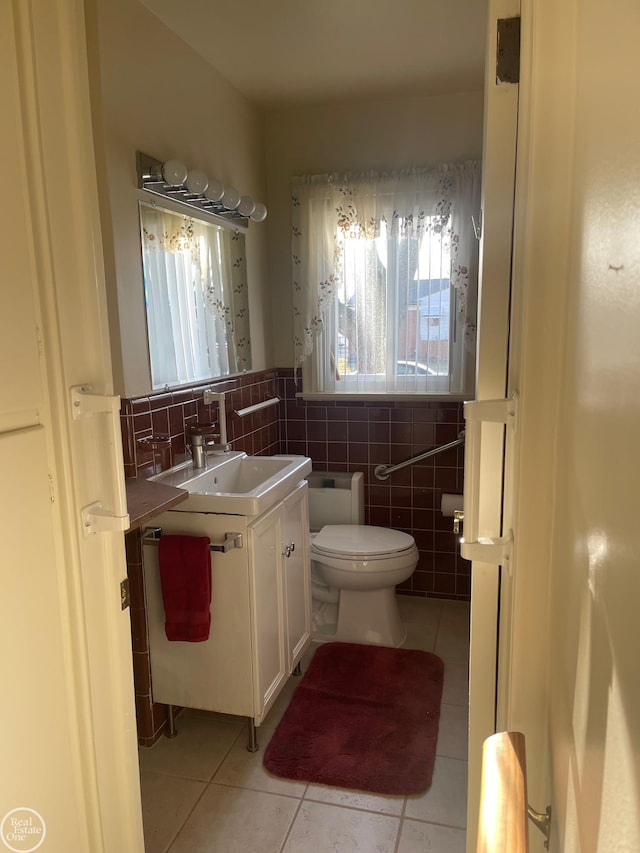 half bath featuring tile patterned flooring, vanity, toilet, and tile walls