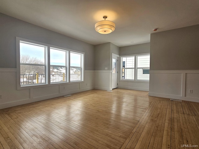 empty room featuring plenty of natural light, wood-type flooring, and wainscoting