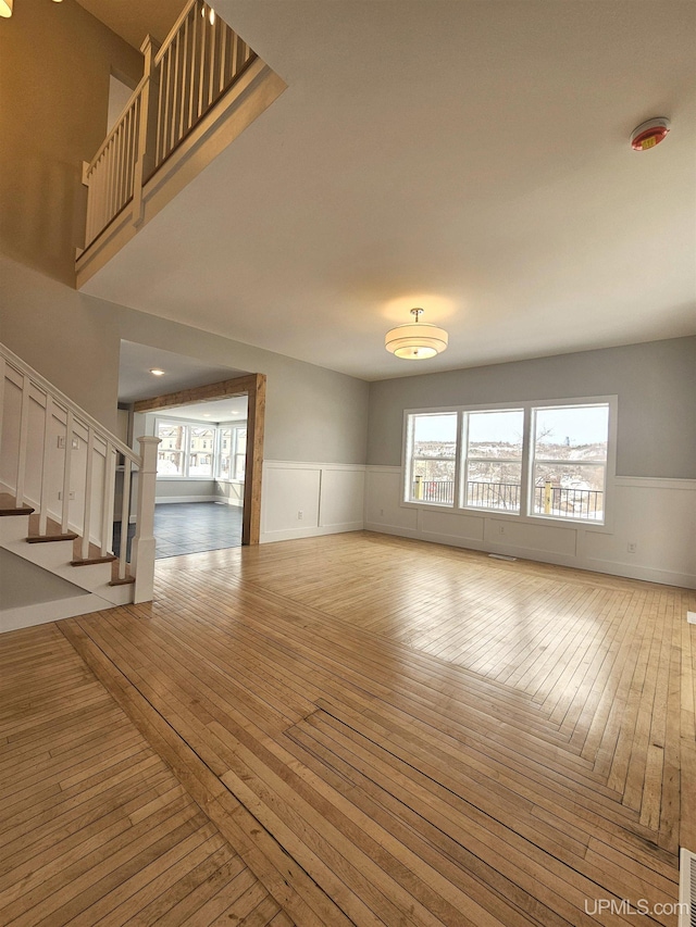 unfurnished living room featuring stairway, visible vents, a wainscoted wall, and light wood-type flooring