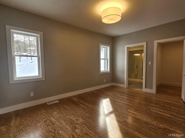 unfurnished bedroom featuring visible vents, connected bathroom, baseboards, and dark wood-style flooring