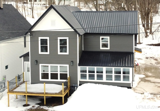 snow covered rear of property with a wooden deck and metal roof