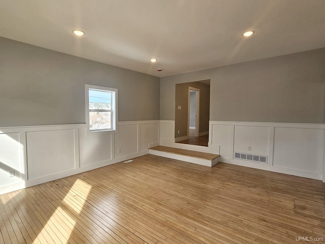 empty room featuring visible vents, recessed lighting, light wood-type flooring, and a wainscoted wall