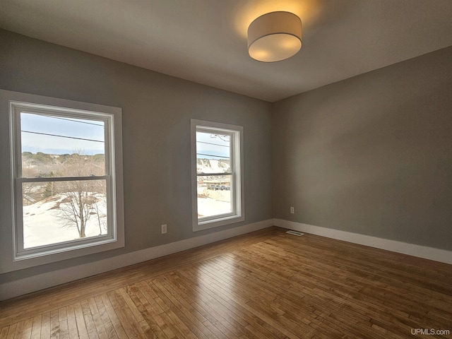 unfurnished room featuring a healthy amount of sunlight, baseboards, and hardwood / wood-style flooring