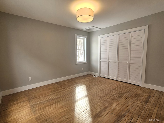 unfurnished bedroom with a closet, visible vents, baseboards, and hardwood / wood-style flooring