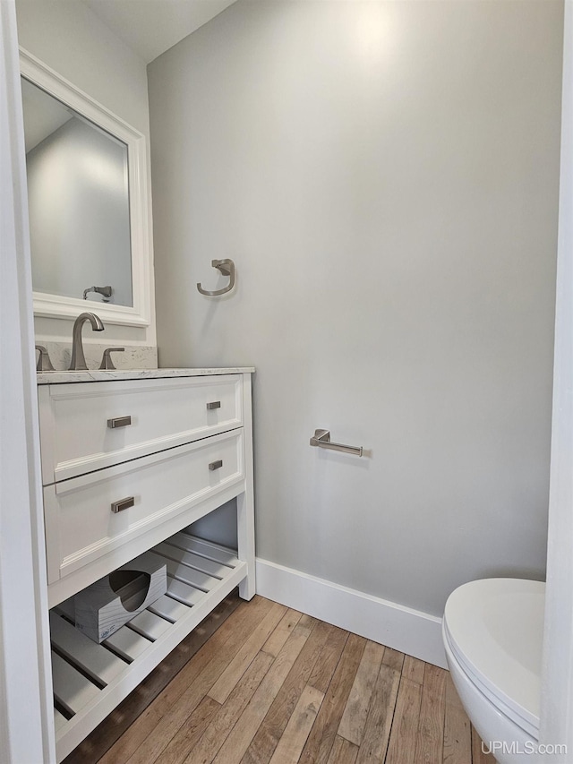 half bathroom with vanity, toilet, wood finished floors, and baseboards