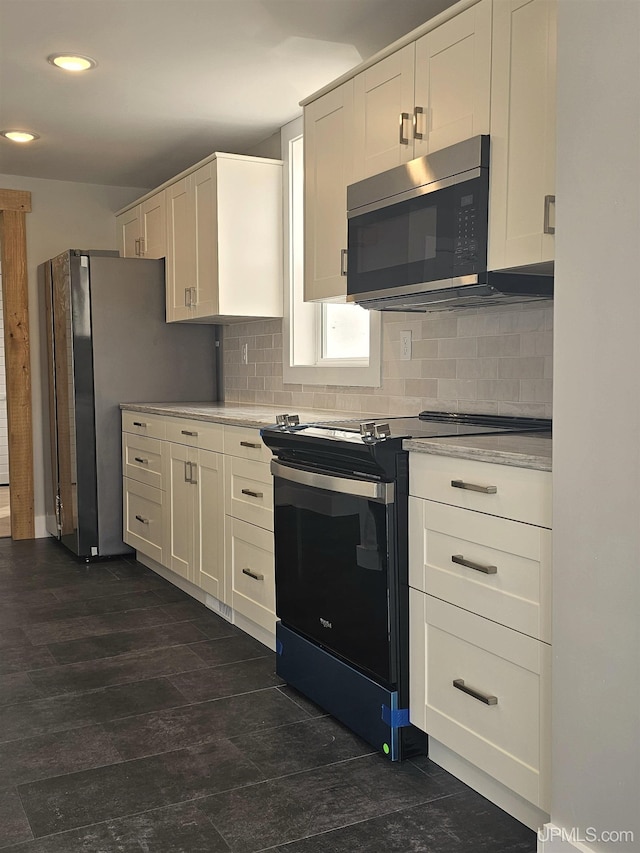 kitchen with electric stove, stainless steel microwave, backsplash, white cabinetry, and light countertops