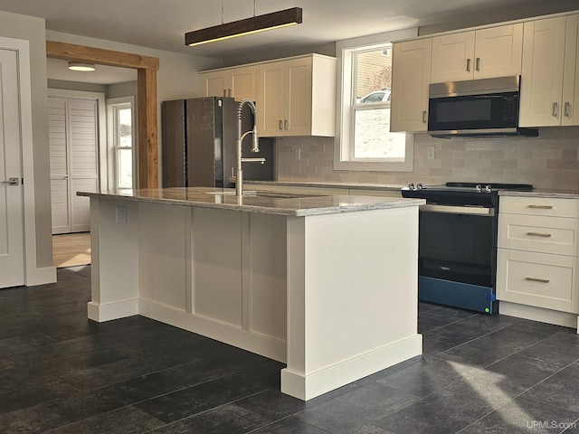 kitchen with a kitchen island with sink, light stone counters, white cabinetry, gas stove, and freestanding refrigerator