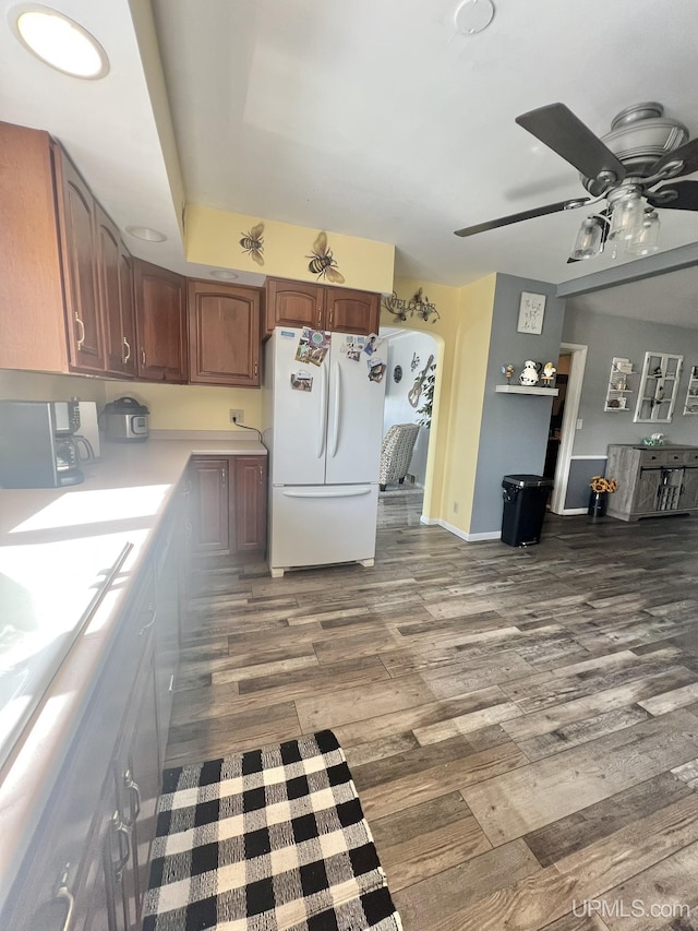 kitchen featuring a ceiling fan, wood finished floors, freestanding refrigerator, arched walkways, and light countertops