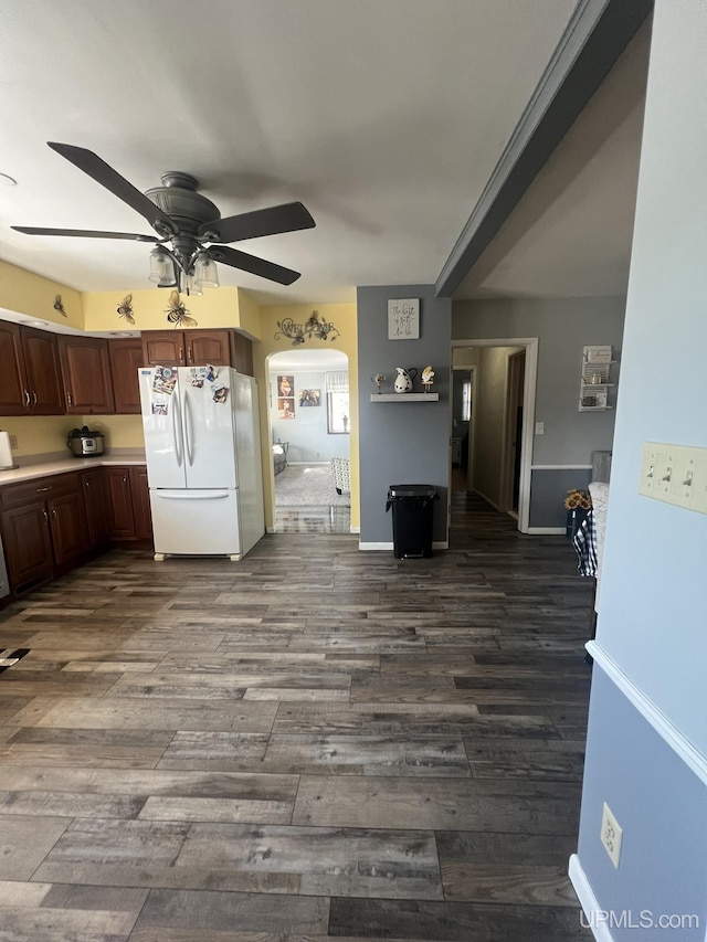 kitchen with freestanding refrigerator, arched walkways, light countertops, ceiling fan, and dark wood-style flooring