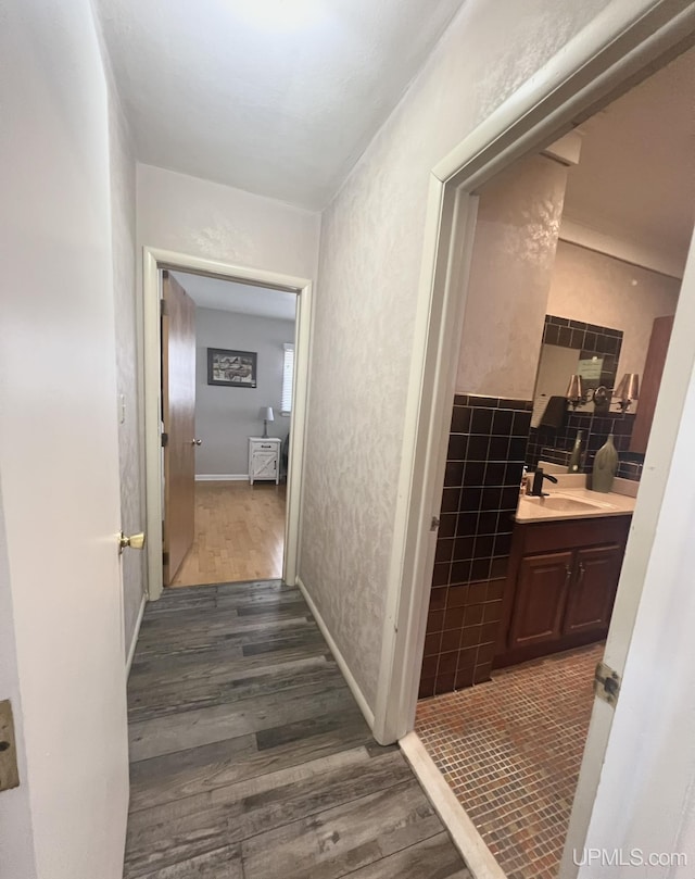 corridor featuring dark wood finished floors, tile walls, a textured wall, and a sink