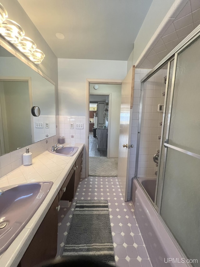 full bathroom featuring tile walls, double vanity, combined bath / shower with glass door, and a sink